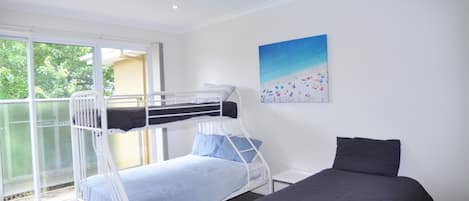 Ein Zimmer mit Etagenbetten, einem Einzelbett und einem großen Fenster mit Blick auf Grünflächen.