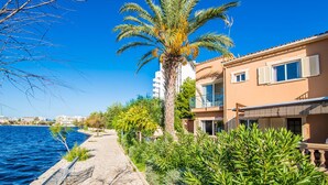 A coastal building with a balcony, a palm tree, and a stone pathway by the sea. - House mountain view Lago Miguel in Alcudia (Alcúdia)