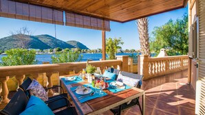 A wooden deck with a table set for dining, overlooking a body of water and hills. - House mountain view Lago Miguel in Alcudia (Alcúdia)