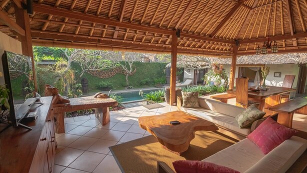 A covered outdoor seating area with a pool, wooden furniture, and a view of the garden. - Ubud Serendipity Villa (Ubud)