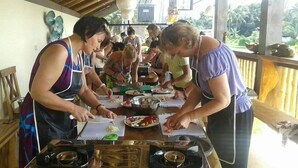 A group of people preparing food at a wooden table with a gas stove and various cooking utensils. - Ubud Serendipity Villa (Ubud)