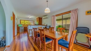 A spacious kitchen with wooden cabinets, a dining area with a wooden table and chairs, and a large window providing natural light. - Driftwood On Anderson - Free Wifi (INVERLOCH)