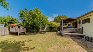 A fenced backyard with a small shed, a covered patio, and a large tree.