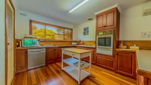 A kitchen with wooden cabinets, a microwave, a dishwasher, a wooden table, and a built-in oven. - Driftwood On Anderson - Free Wifi (INVERLOCH)