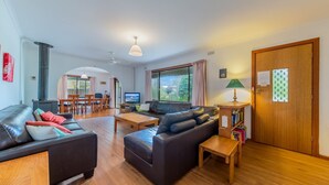 A living room with a sofa, a coffee table, and a TV. There is a wooden door and a window with curtains. - Driftwood On Anderson - Free Wifi (INVERLOCH)