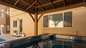Ein Wellnessbereich mit einem gläsernen Whirlpool, Holzbalken und einem Fenster mit Jalousien.