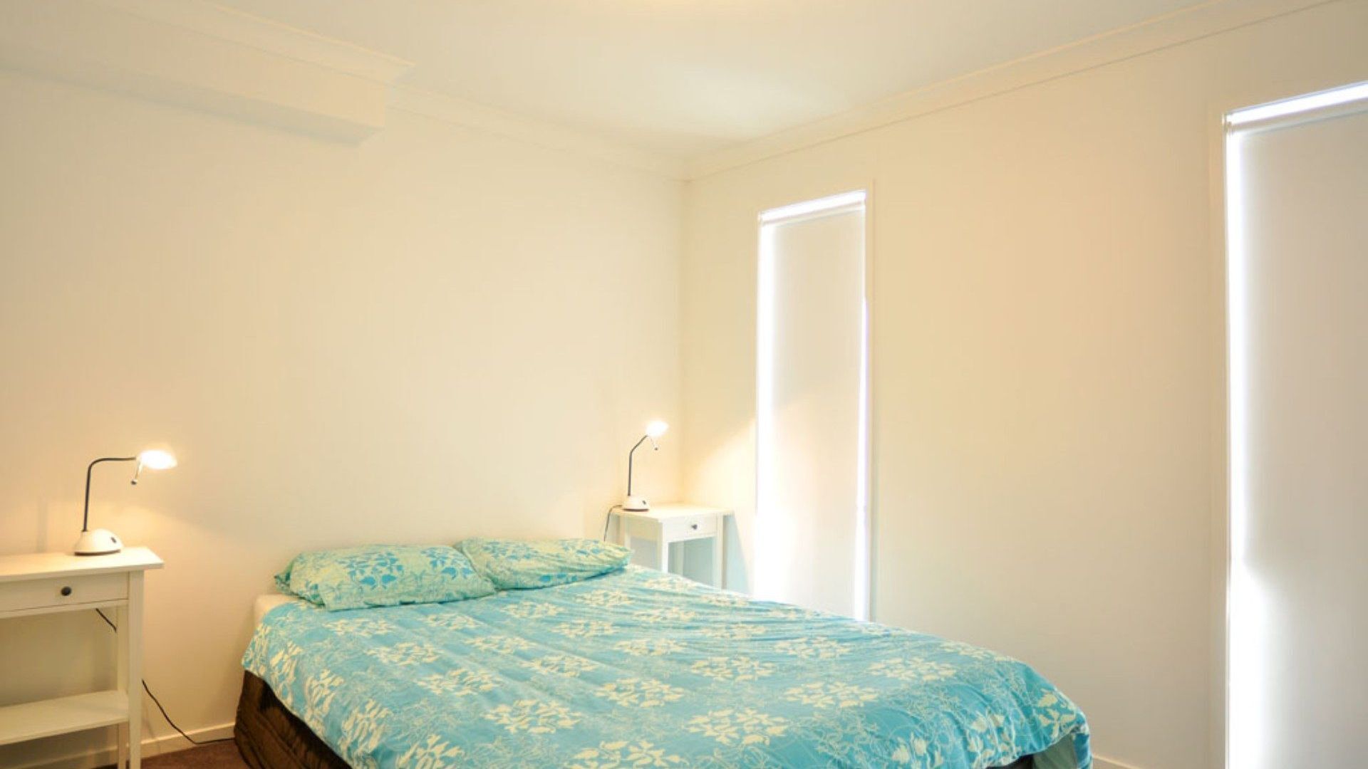 A bedroom with a bed, two bedside tables, and a window.