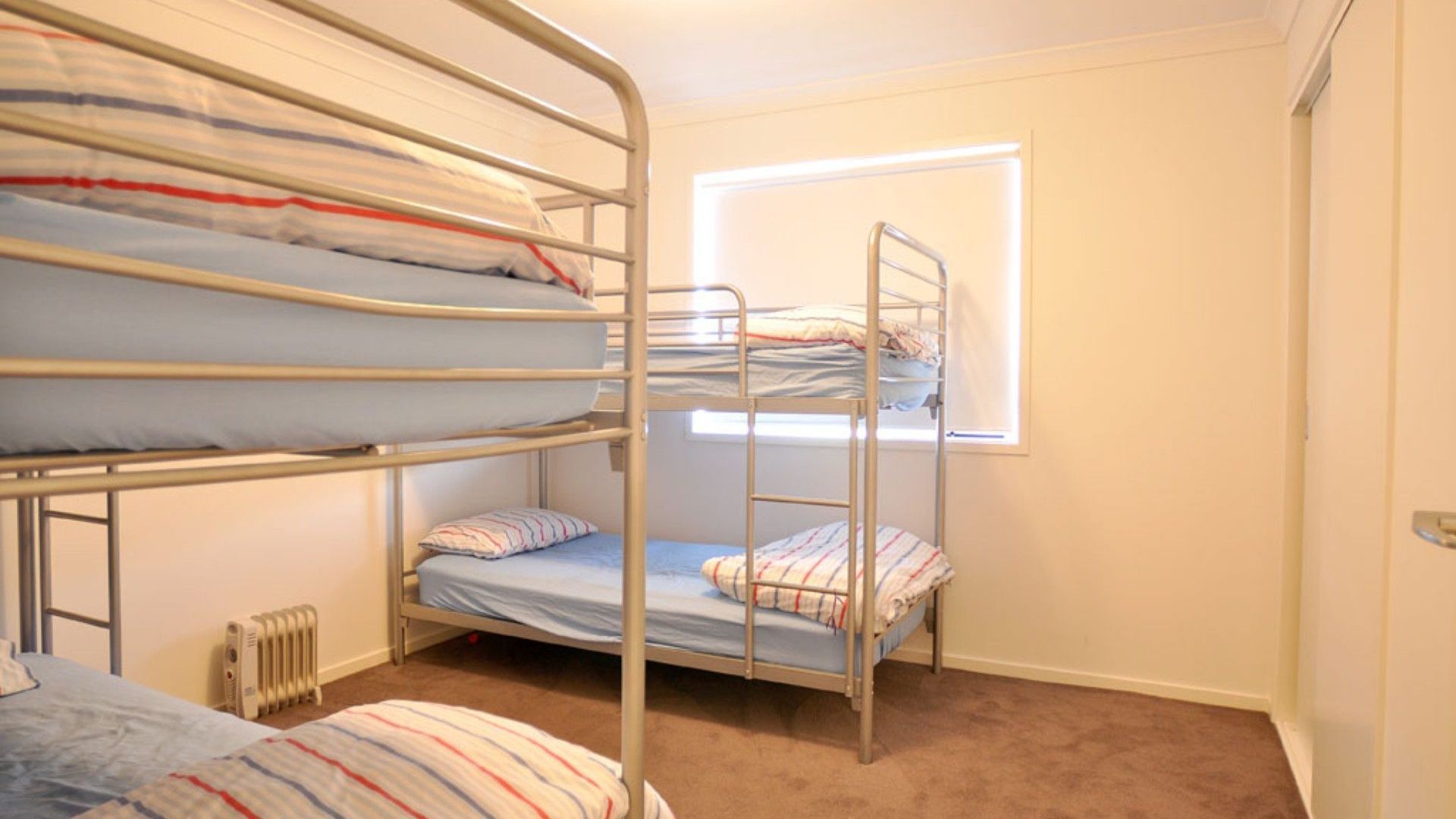 A dormitory room with bunk beds, a radiator, and a window with blinds.