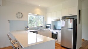 Una cocina moderna con armarios blancos, un refrigerador de acero inoxidable, un microondas y una tetera sobre la encimera.