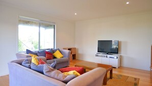 Una sala de estar moderna con un sofá gris, una mesa de centro de madera y un televisor de pantalla plana sobre un soporte blanco.
