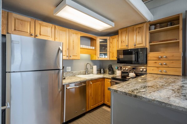 A modern kitchen with wooden cabinets, stainless steel appliances, a granite countertop, and a built-in microwave.