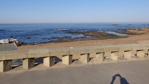 Carretera costera con barandilla, costa rocosa y mar tranquilo.