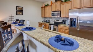 Een moderne keuken met granieten aanrecht, houten kastjes, roestvrijstalen apparatuur en een ontbijtbalk met blauwe placemats.