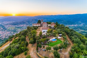 An aerial view of a historic building complex with a church, a bell tower, and surrounding greenery.