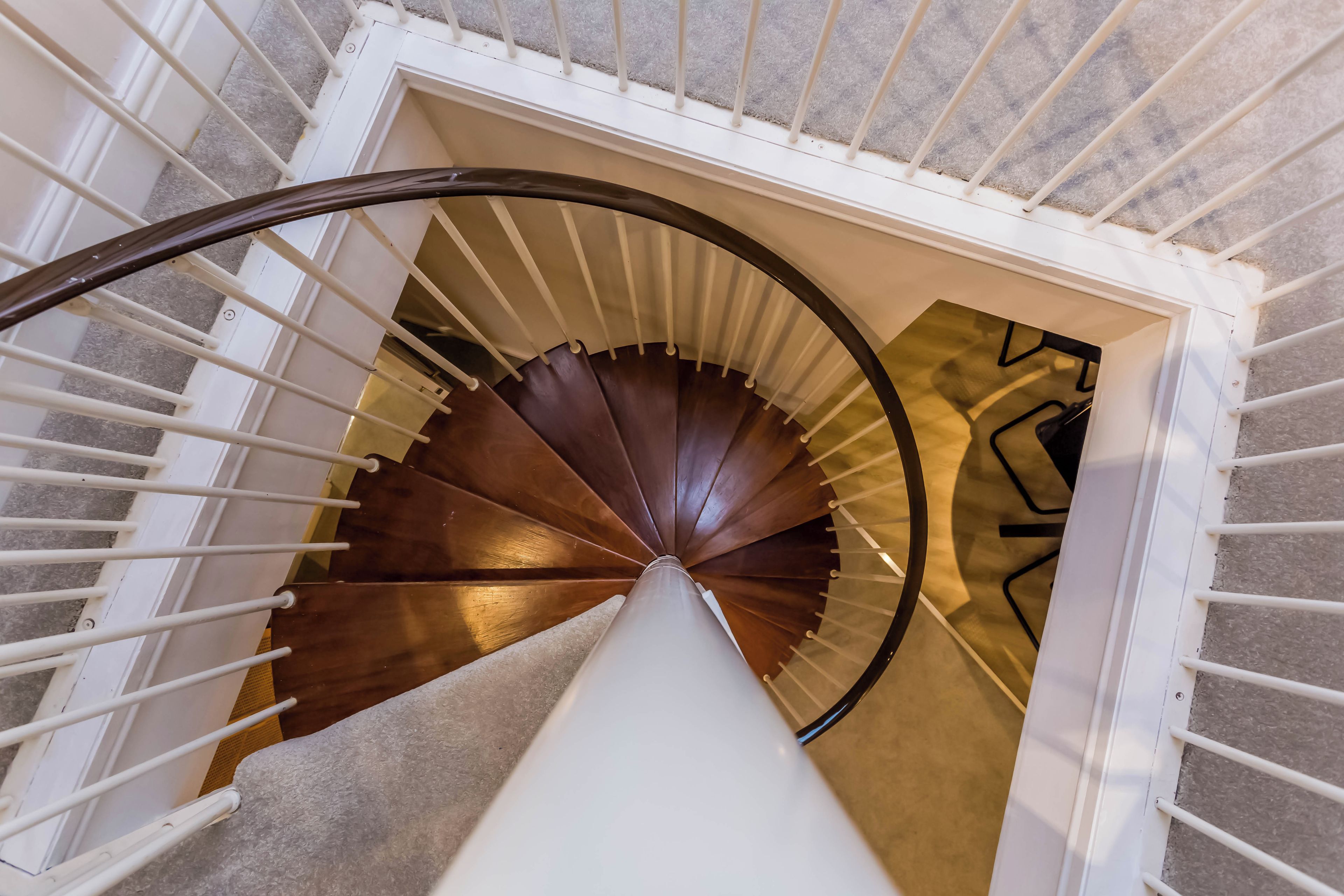 A spiral staircase with white railings and a wooden finish, leading to an upper floor.
