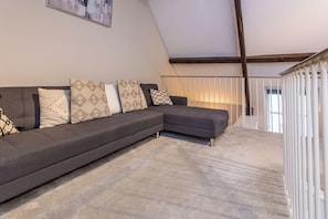 Un salon moderne avec un canapé d’angle, des coussins à motifs et une vue sur un balcon.