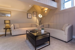 A modern living room with a sectional sofa, a glass coffee table, a floor lamp, and framed artwork on the wall.