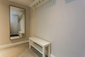 A hallway with a white bench, a full-length mirror, and a door leading to a staircase.