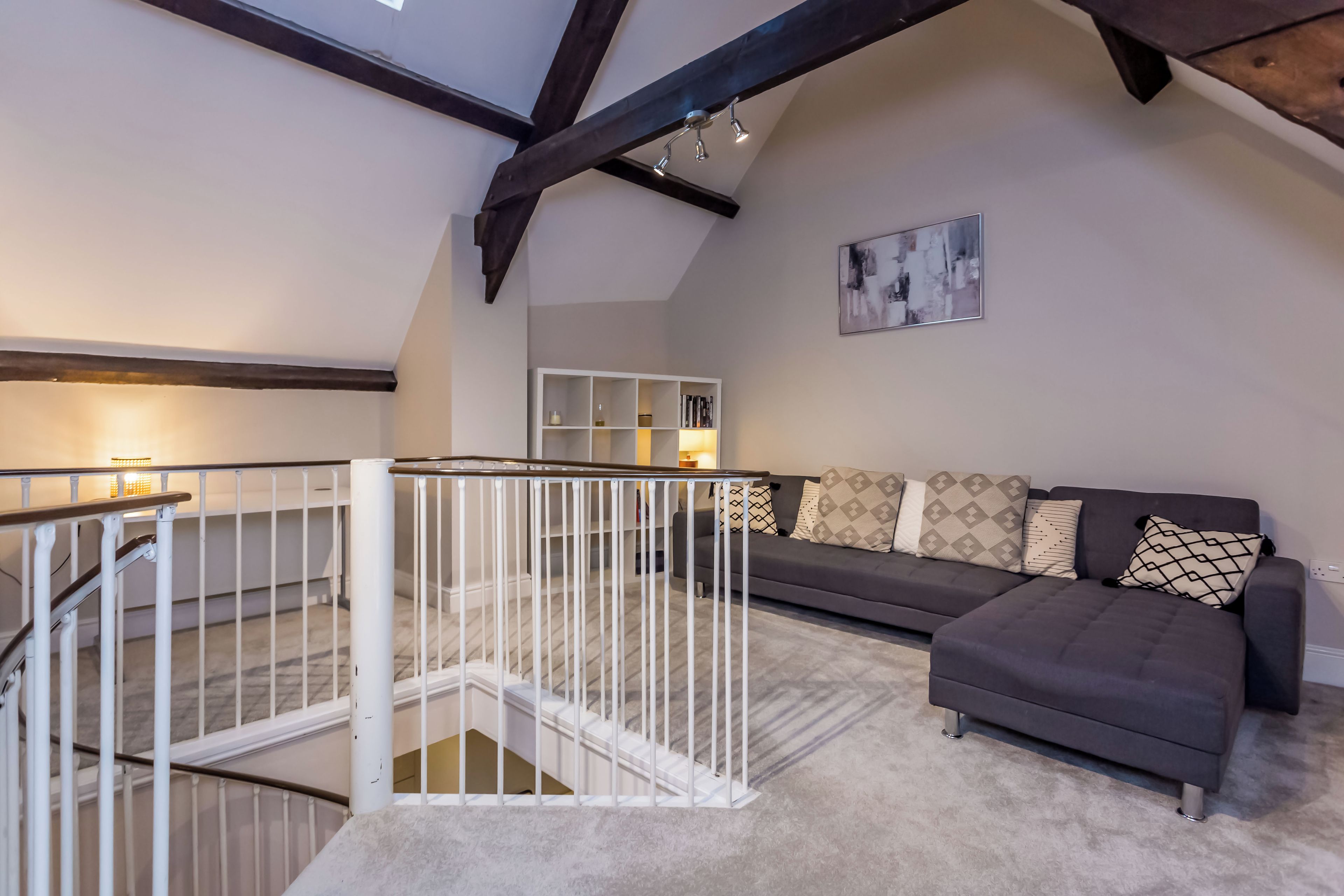 A modern living room with a grey sofa, a white railing, and a staircase leading to an upper level.