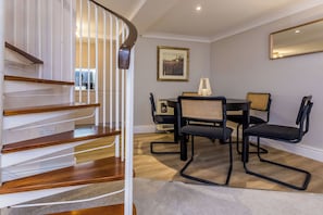 A staircase with wooden steps and white railings leading to a room with a dining table, chairs, and a framed picture on the wall.