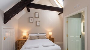 Un dormitorio con una cama grande, dos mesitas de noche con lámparas, una viga de techo de madera y una puerta blanca.