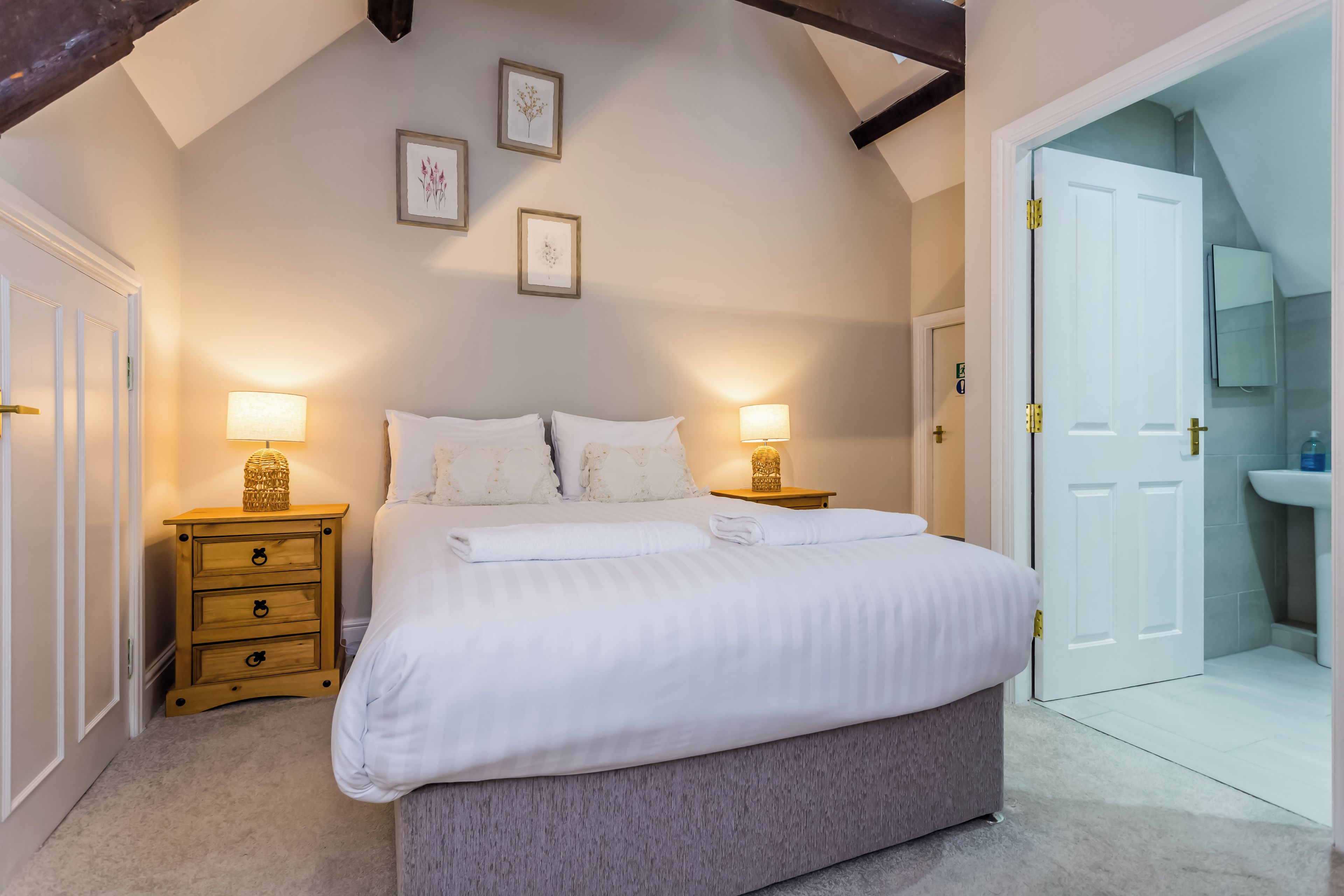 Une chambre à coucher avec un lit, des tables de chevet, une armoire et une salle de bain visible à travers une porte ouverte.