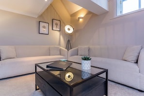 A modern living room with a glass coffee table, two sofas, a floor lamp, and framed artwork on the wall.