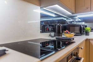 A modern kitchen with a black induction cooktop, a coffee machine, and a basket of items on the counter.