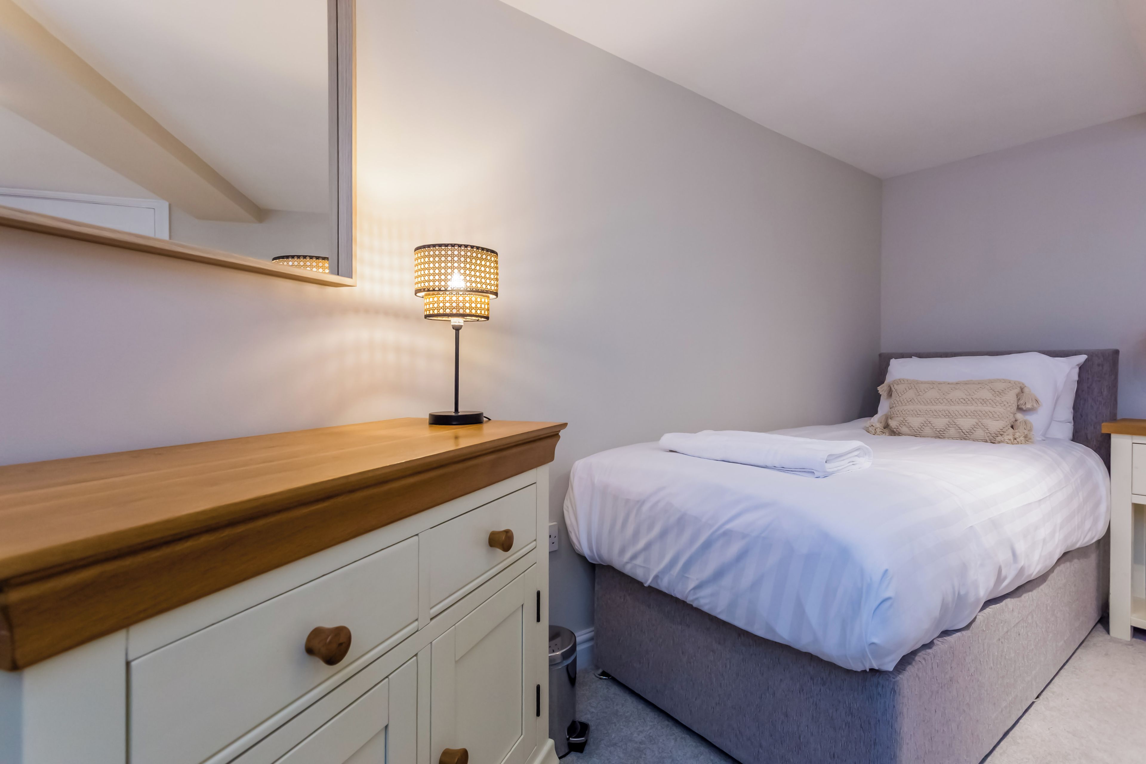 A bedroom with a bed, bedside table, lamp, and a dresser with drawers.