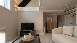 Una sala moderna con un televisor de pantalla plana, una mesa de centro de vidrio, un sofá color beige y una mesita auxiliar de mimbre.
