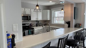 A modern kitchen with white cabinets, stainless steel appliances, and a bar area with black chairs.