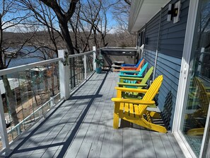 Eine Holzterrasse mit Geländer, eine Reihe bunter Adirondack-Stühle und Blick auf einen See und Bäume.