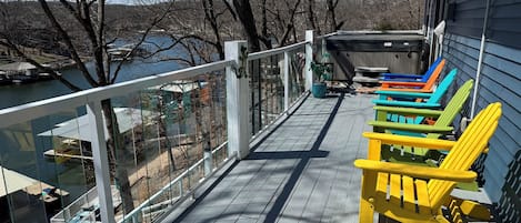 Eine Holzterrasse mit Geländer und Blick auf ein Gewässer, farbenfrohe Adirondack-Stühle sowie ein See und Bäume.