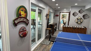A room with a ping pong table, a foosball table, and a glass door leading to an outdoor patio.