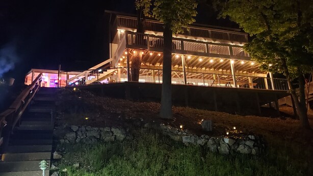 A multi-level wooden building with outdoor lighting, a staircase, and a stone retaining wall.