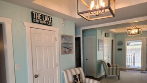 A hallway with a striped armchair, a door with a sign reading "THE LAKE IS MY HAPPY PLACE," and a large mirror reflecting the room.