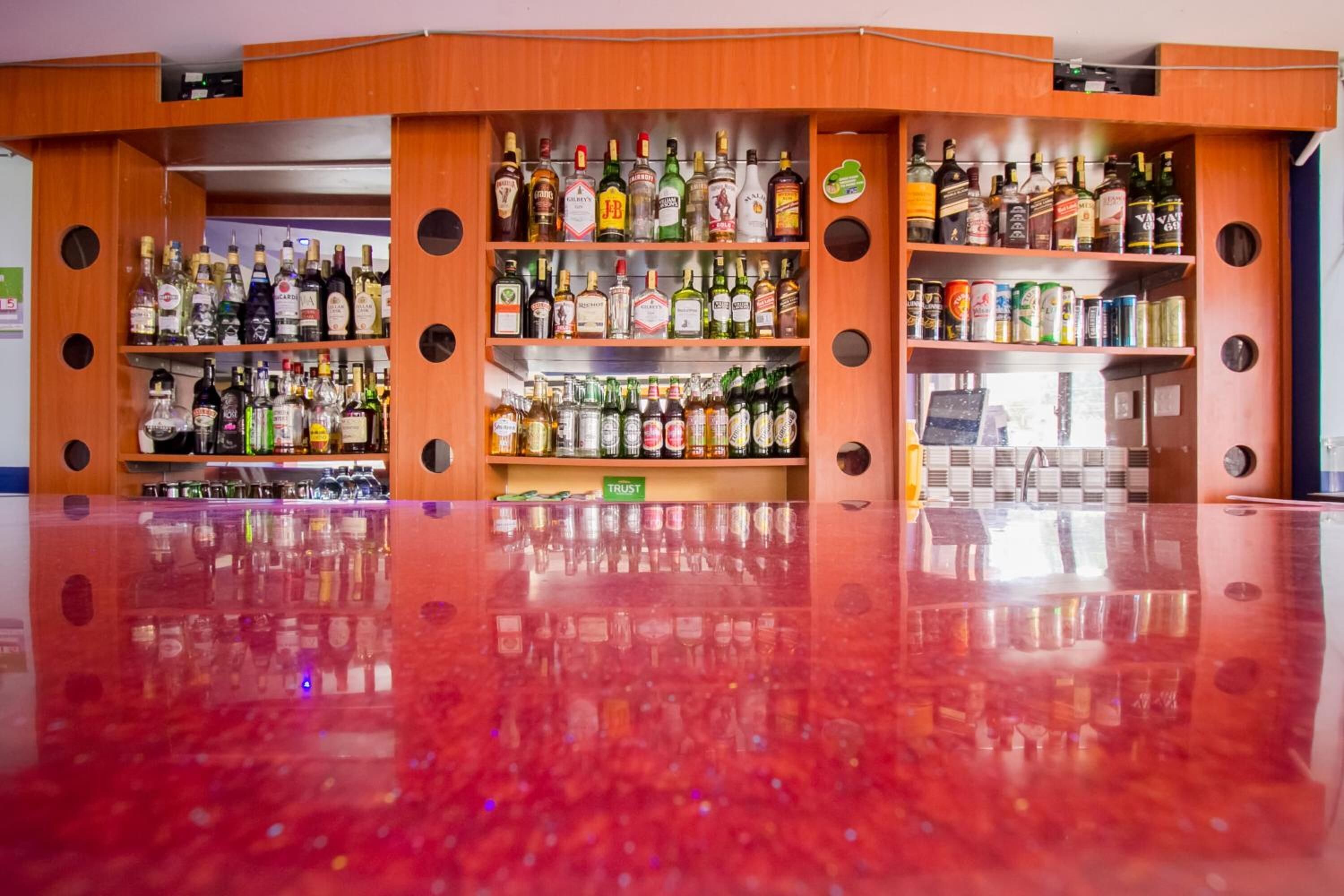 A bar with multiple shelves of liquor bottles, a polished red floor, and a 'TRUST' sign on the counter.