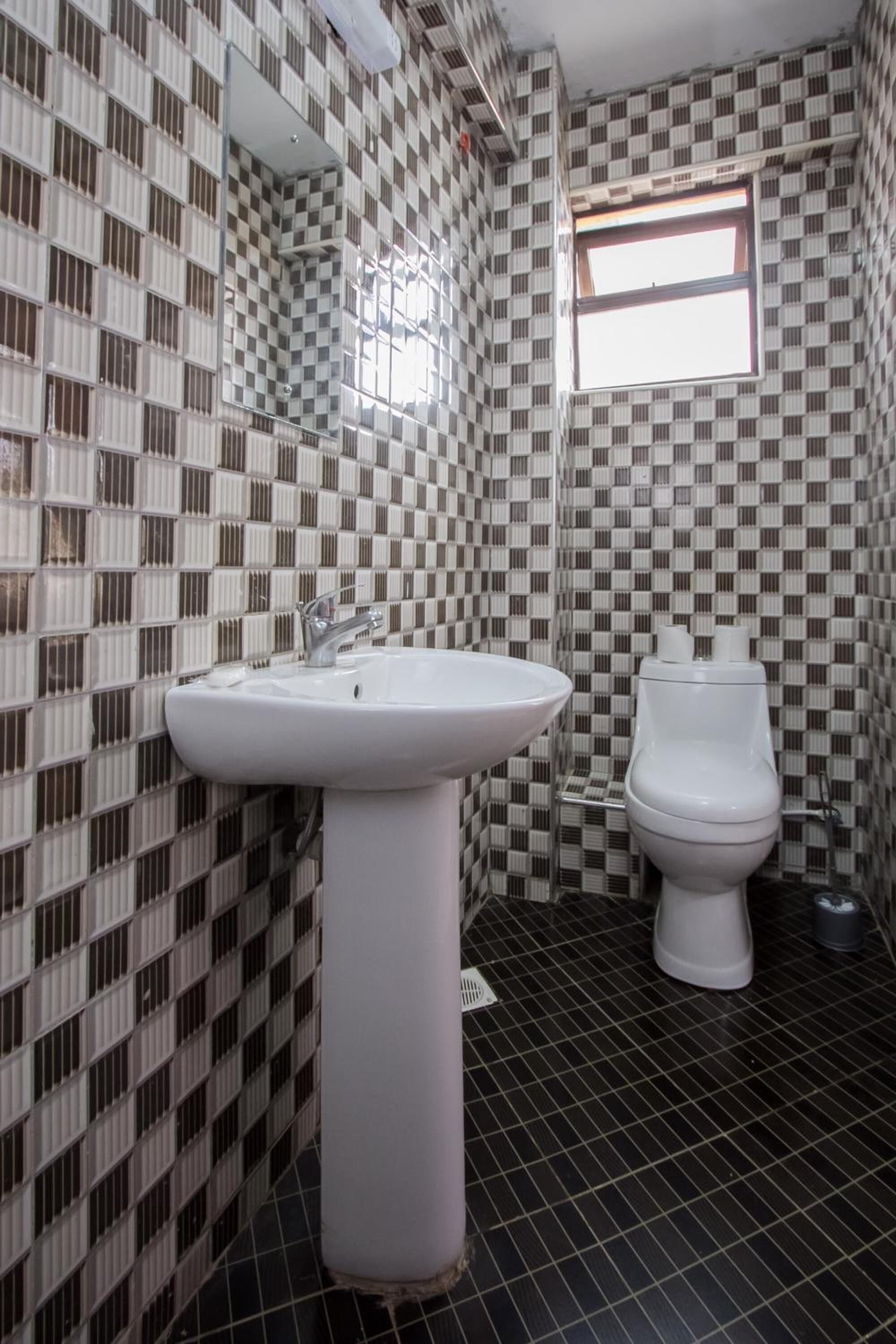 A bathroom with a checkered tile pattern on the walls and floor, a white sink, and a toilet.