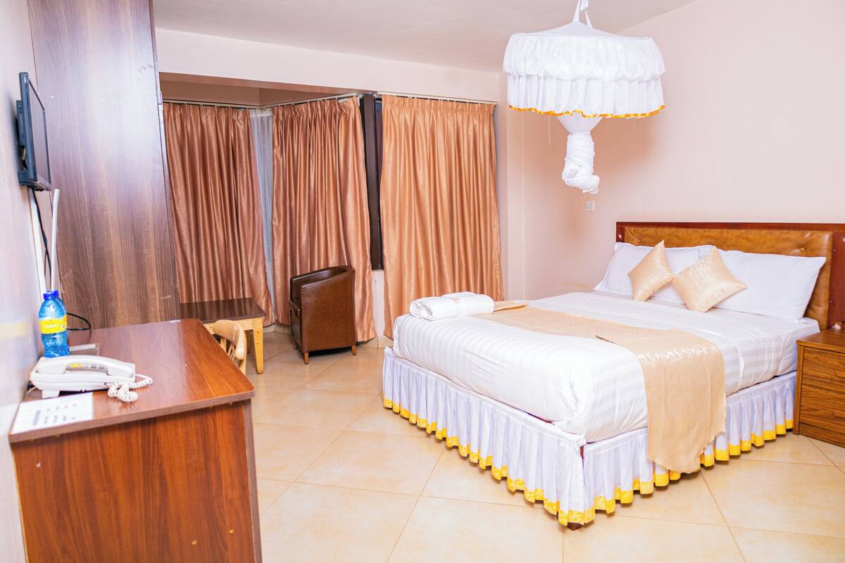A hotel room with a bed, a desk with a telephone, a chair, and a curtain.