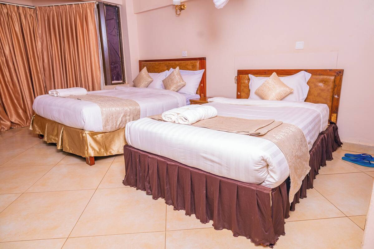 A hotel room with two beds, each with a wooden headboard, white linens, and a brown skirt.