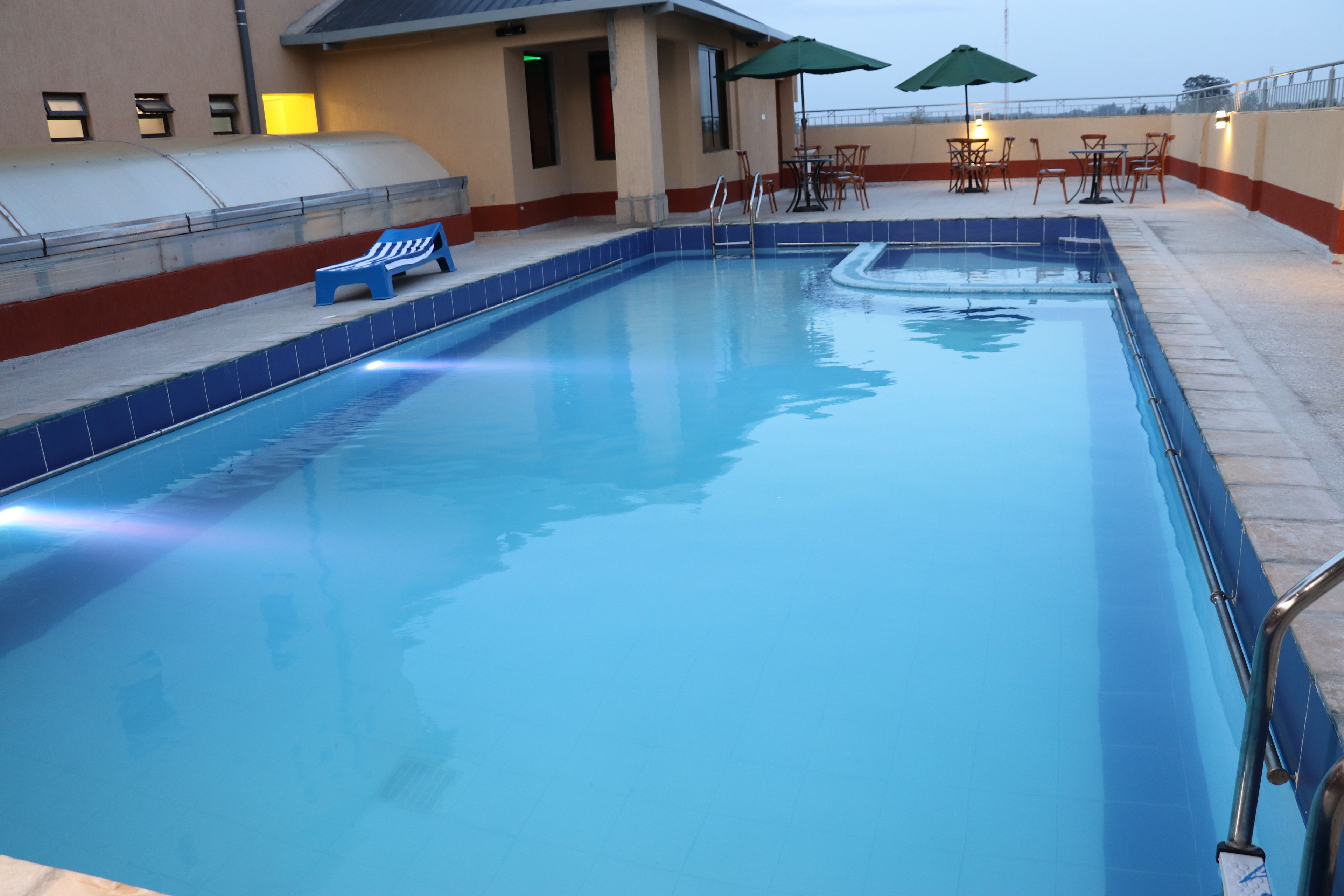 Ein Pool mit Liegestühlen und Sonnenschirmen, umgeben von einer überdachten Terrasse mit Tischen und Stühlen.