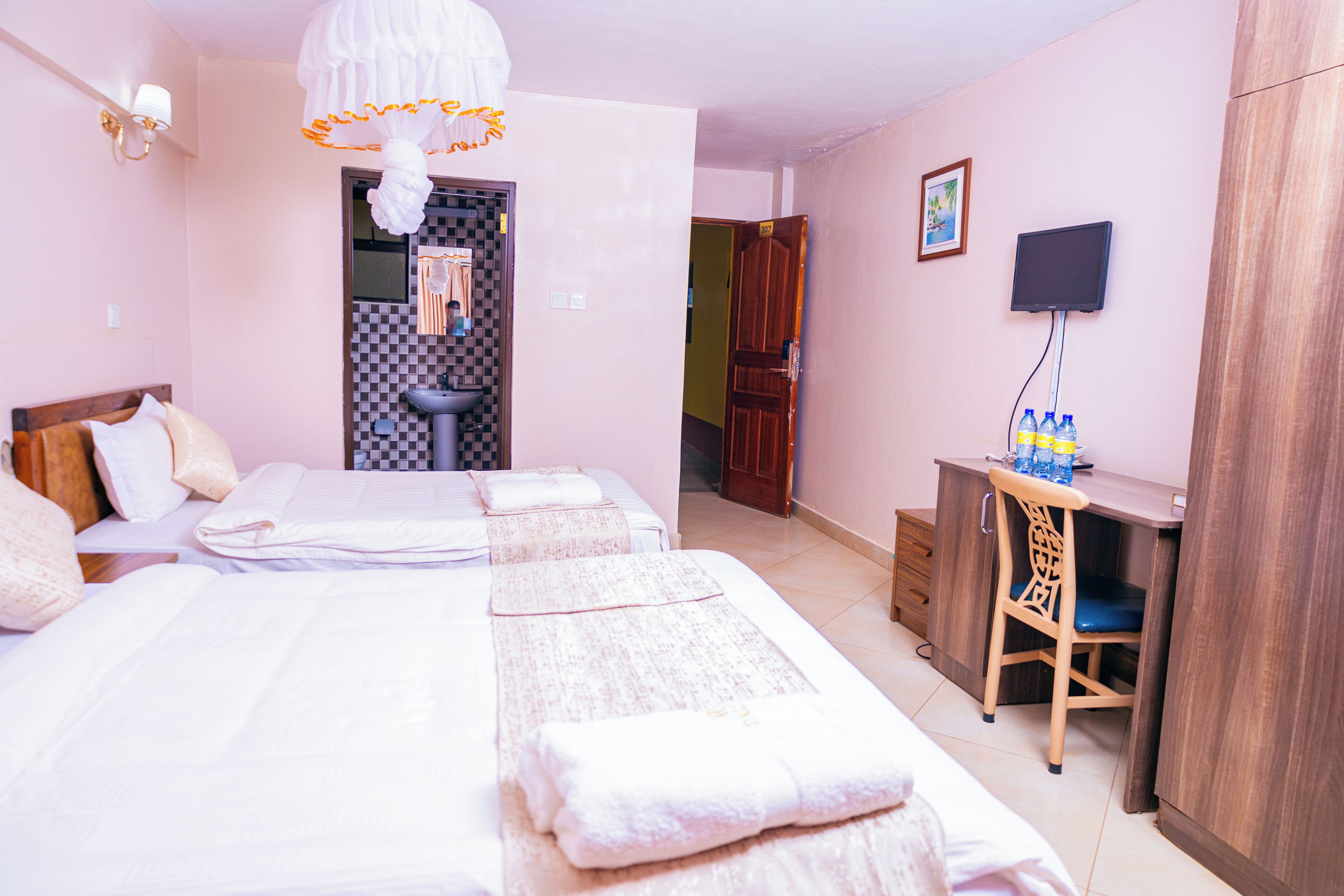 Habitación de hotel con dos camas, un escritorio, una silla, un televisor y un baño visible a través de una puerta abierta.