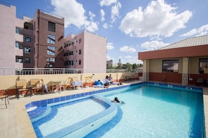 A swimming pool with lounge chairs and a sunbathing area, surrounded by buildings.