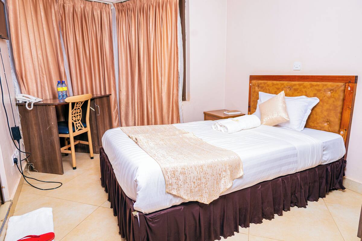 A hotel room with a bed, a desk, a chair, and curtains.