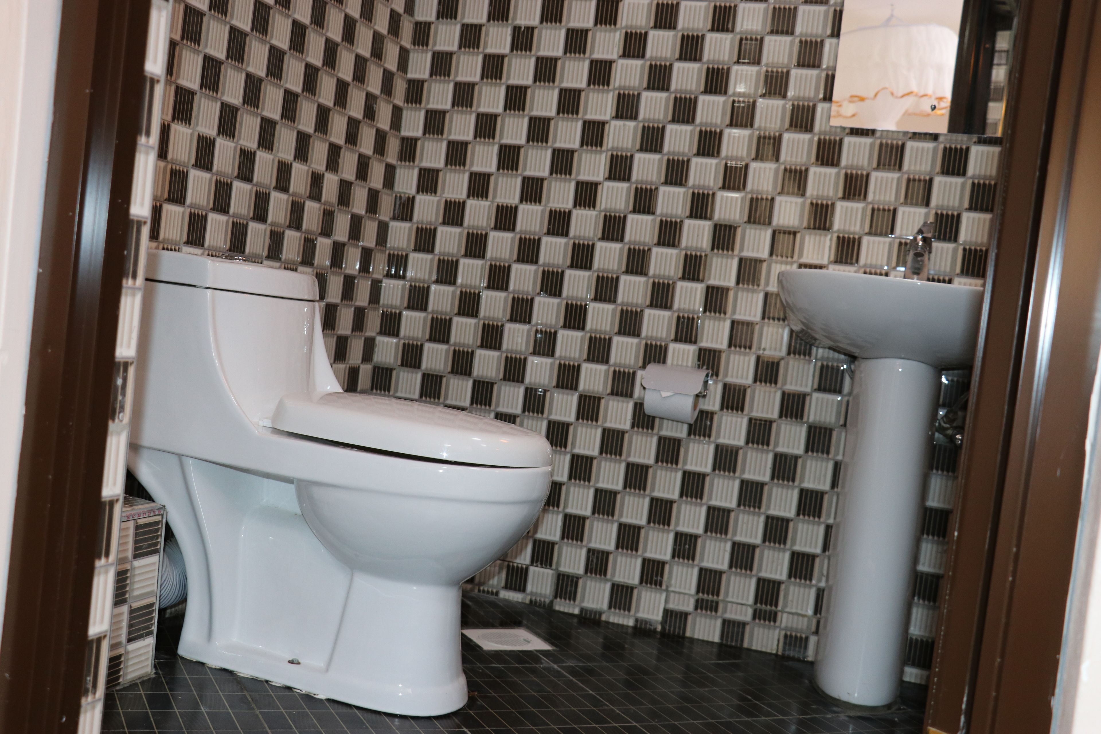 A bathroom with a toilet and sink, checkered tile backsplash, and a mirror.