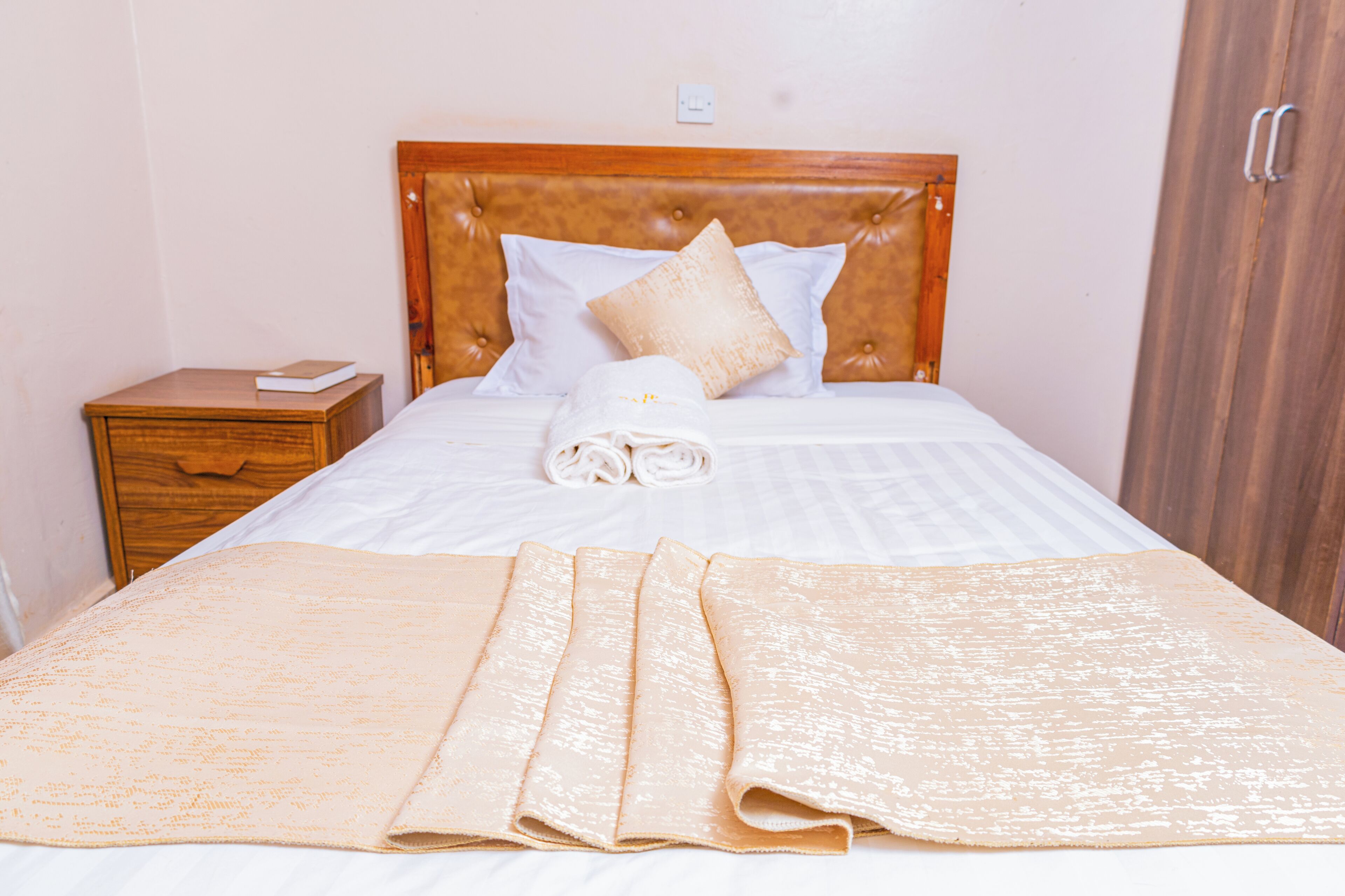 A neatly made bed with a wooden headboard, white linens, and a beige blanket.