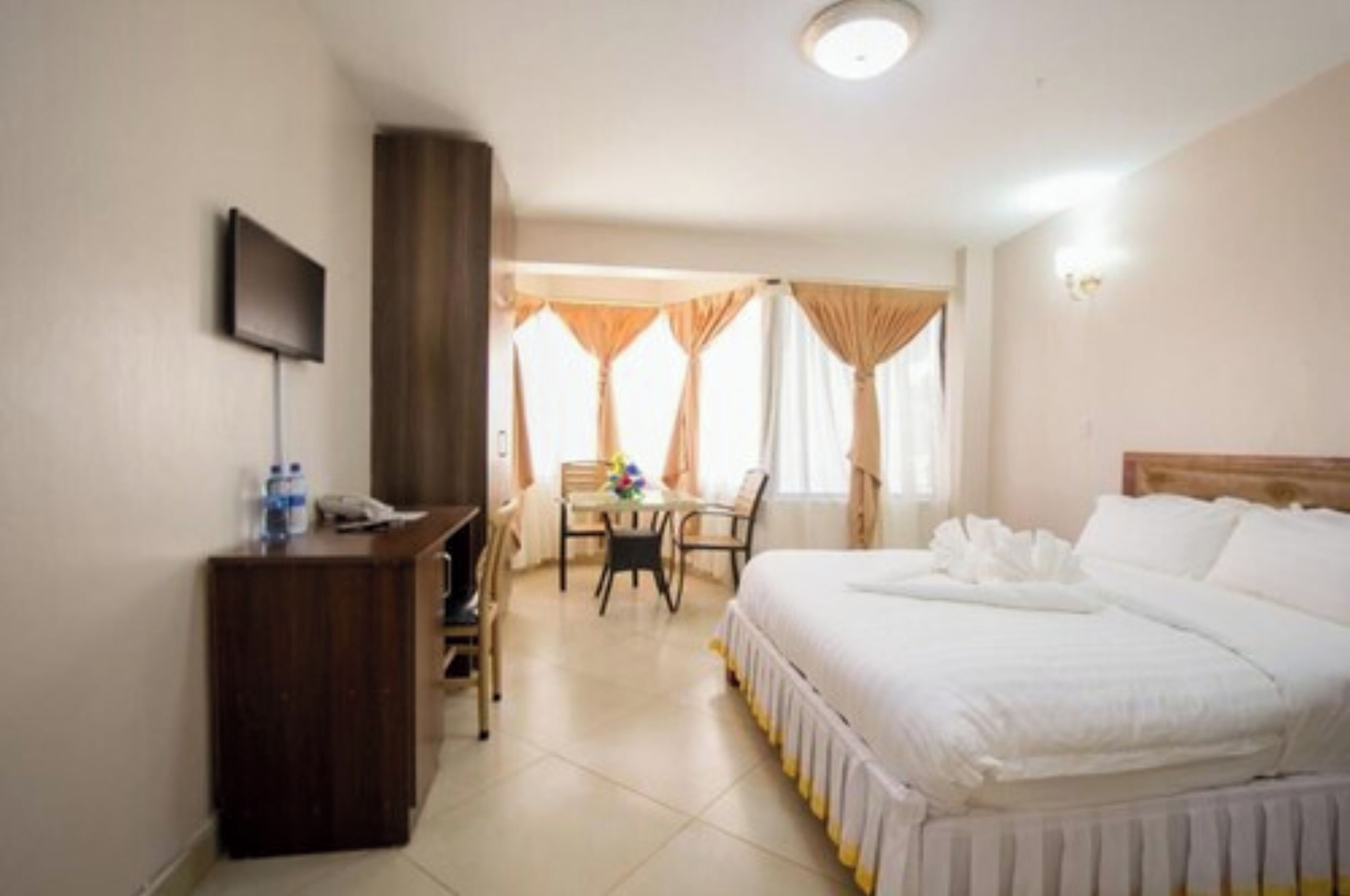 A hotel room with a bed, a desk, a chair, a television, and a window with curtains.
