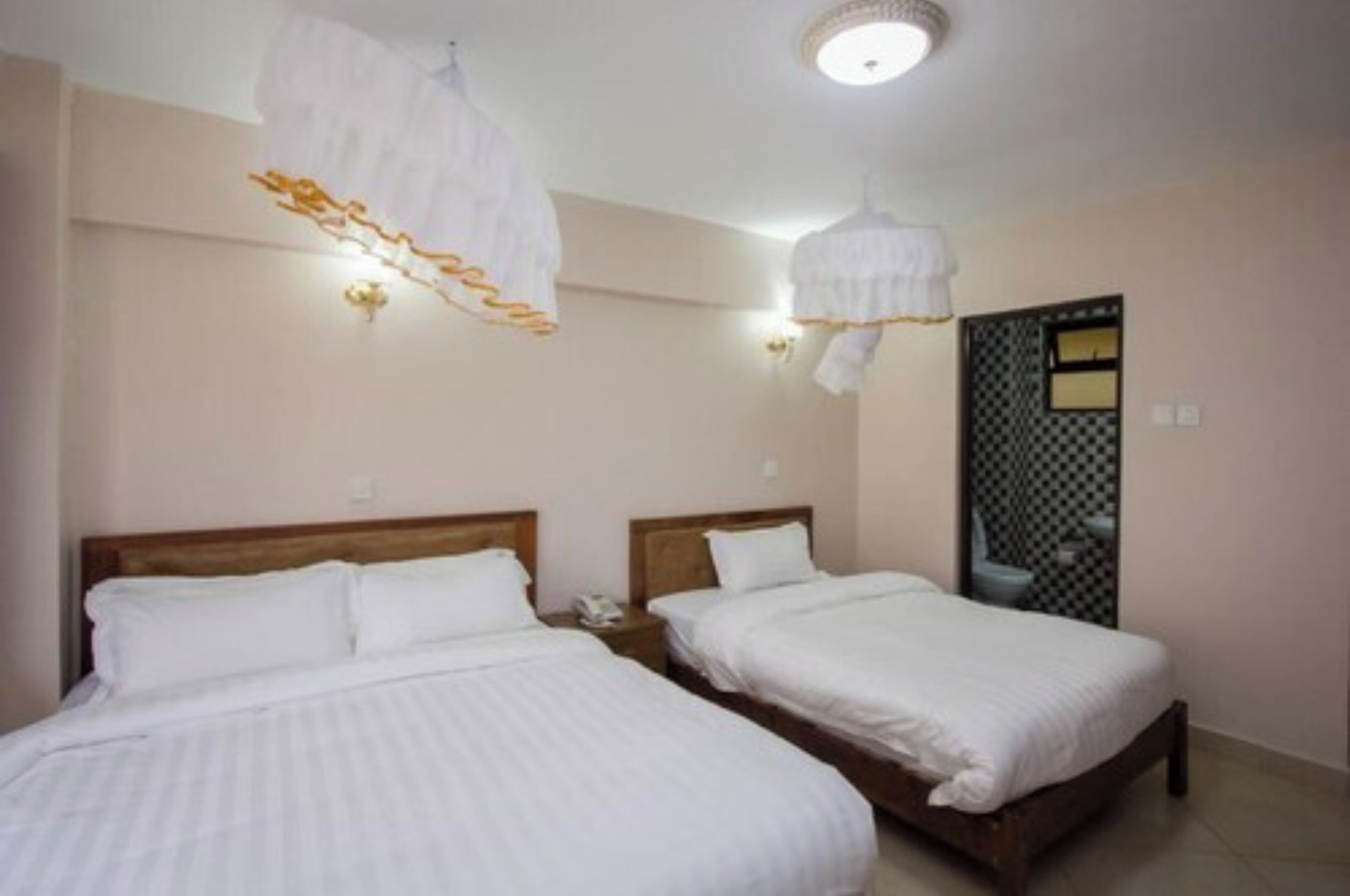 Una habitación de hotel con dos camas individuales, un cabecero de madera, una pared blanca y una lámpara decorativa.
