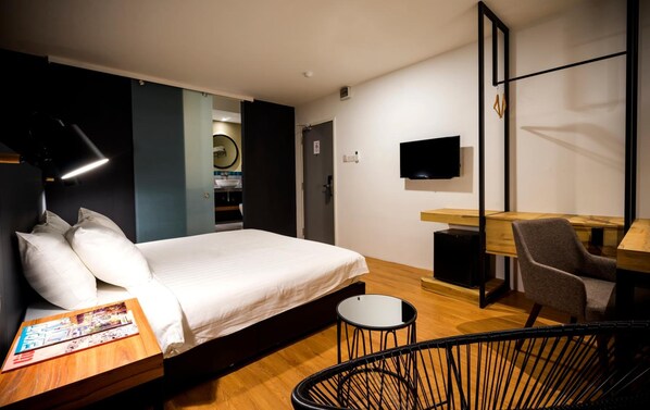 A modern hotel room with a bed, a desk, a chair, a TV, and a small round table.