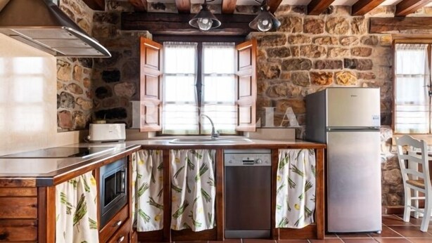 A rustic kitchen with stone walls, wooden beams, a built-in oven, a sink, and a refrigerator. - Casa Ángela - country house in Villanueva de la Peña (Cantabria) | 6 guests (Villanueva De La Peña)